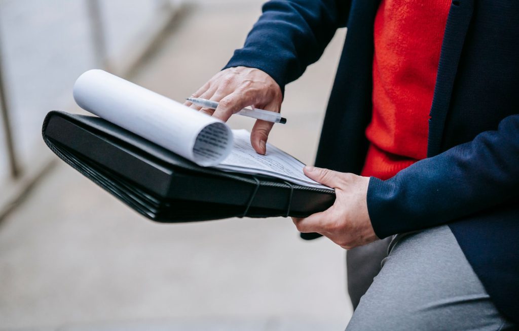 Close-up of a professional person reviewing documents outdoors. Engaged in work with focus on writing materials. — A Brief Gu
