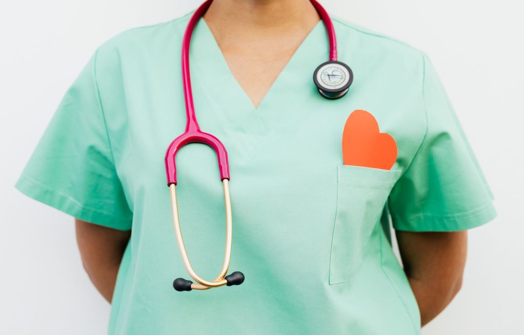 Close-up of a medical professional with a stethoscope and a paper heart cutout on a green uniform pocket. — Benefits of Onlin