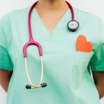 Close-up of a medical professional with a stethoscope and a paper heart cutout on a green uniform pocket. — Benefits of Onlin