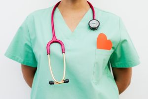 Close-up of a medical professional with a stethoscope and a paper heart cutout on a green uniform pocket. — Benefits of Onlin