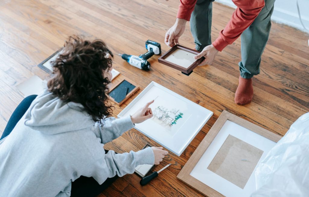 A couple organizing picture frames on a wooden floor, preparing for interior decoration or renovation. — Exploring Different