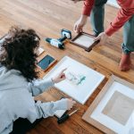 A couple organizing picture frames on a wooden floor, preparing for interior decoration or renovation. — Exploring Different