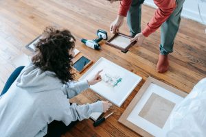 A couple organizing picture frames on a wooden floor, preparing for interior decoration or renovation. — Exploring Different