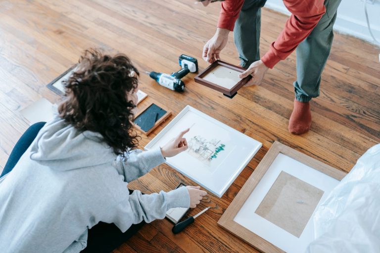 A couple organizing picture frames on a wooden floor, preparing for interior decoration or renovation. — Exploring Different