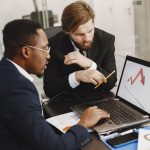 Two business professionals discuss marketing data on a laptop in a modern office. — From Click to Cannabis: A Beginner's Guid