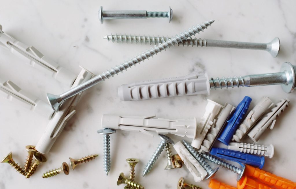 Set of various multicolored plastic dowels with metal screws of different sizes placed on white marble table in modern worksh