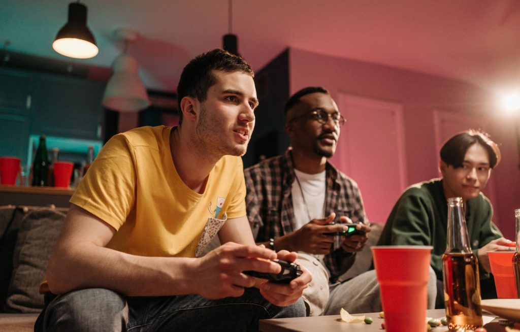 Diverse group of young adults playing video games on a cozy sofa with refreshments. — Play And Download The fun88 app