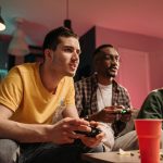 Diverse group of young adults playing video games on a cozy sofa with refreshments. — Play And Download The fun88 app