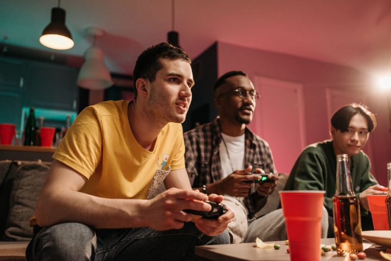 Diverse group of young adults playing video games on a cozy sofa with refreshments. — Play And Download The fun88 app