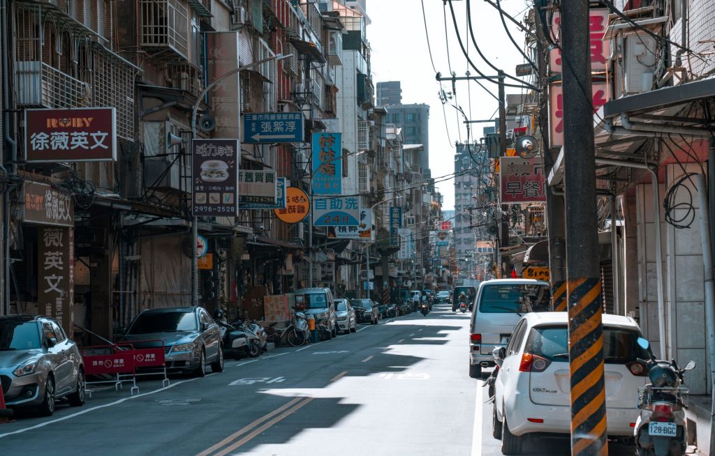 A busy street lined with cars and various colorful business signs on a sunny day. — Urban Oasis of Sensuality: Explore Nuru M