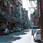 A busy street lined with cars and various colorful business signs on a sunny day. — Urban Oasis of Sensuality: Explore Nuru M